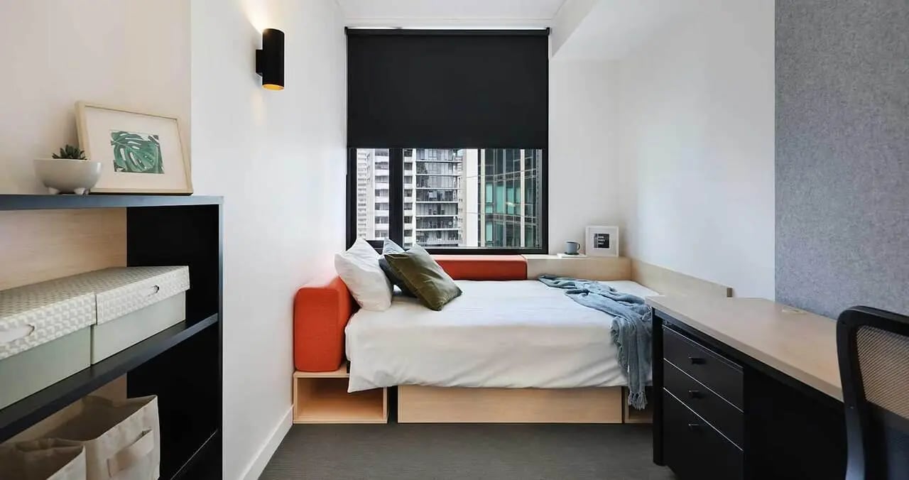 Bed with orange cushions black desk storage Bedroom at Iglu Melbourne City in Melbourne Student Accommodation