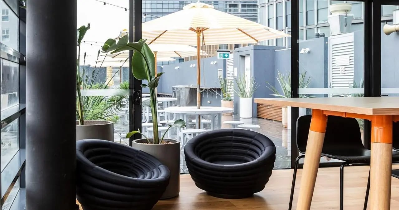 Two black chairs table plants patio umbrellas exterior at Iglu Broadway in Sydney Student Accommodation