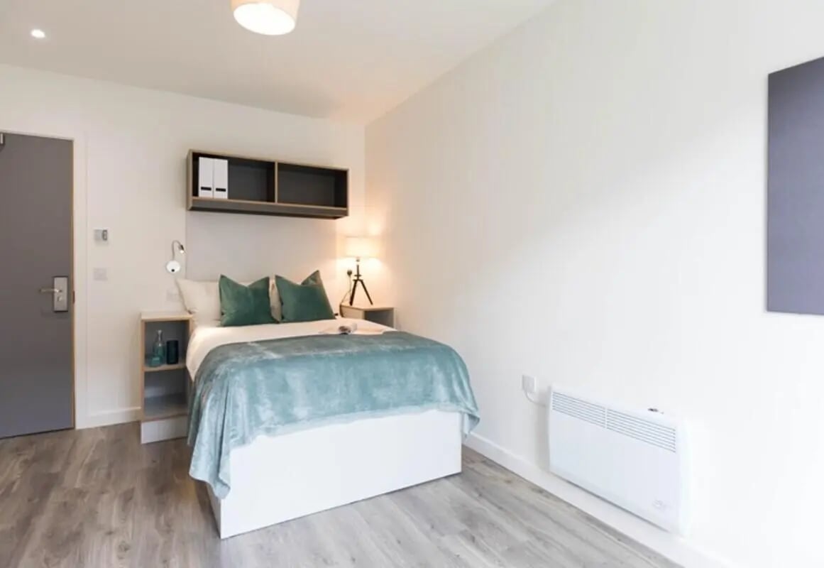 Bed with teal throw green pillows shelves bedroom at The Cam Foundry in Cambridge Student Accommodation