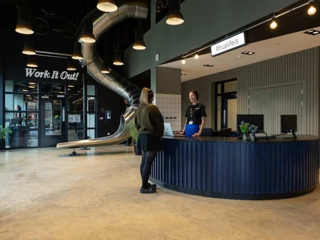 Reception desk with employees and slide exterior at True Manchester-Salford in Salford Student Accommodation