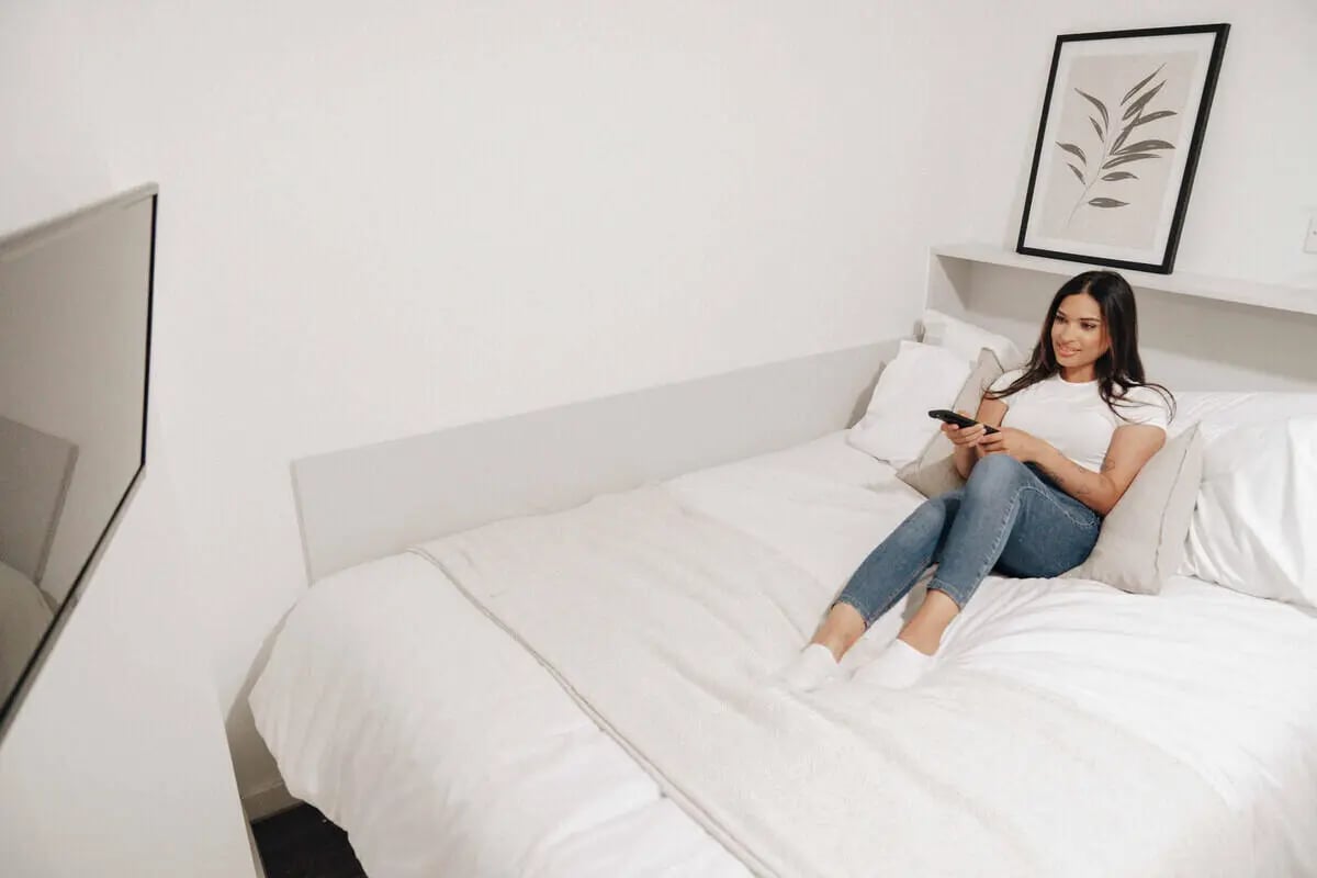 Woman on bed holding remote TV on wall Bedroom at Market House in Newcastle Upon Tyne Student Accommodation