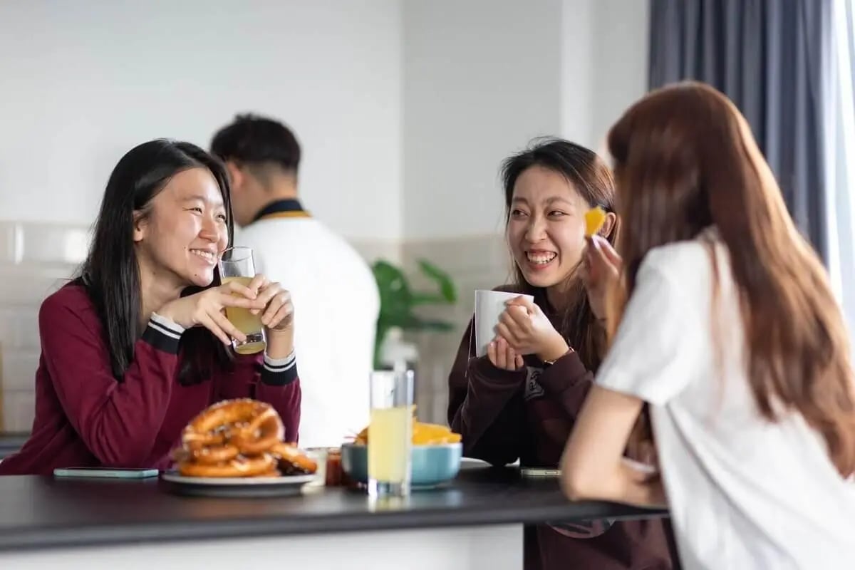 Students chatting with drinks and pretzels kitchen area at West Village in Glasgow Student Accommodation