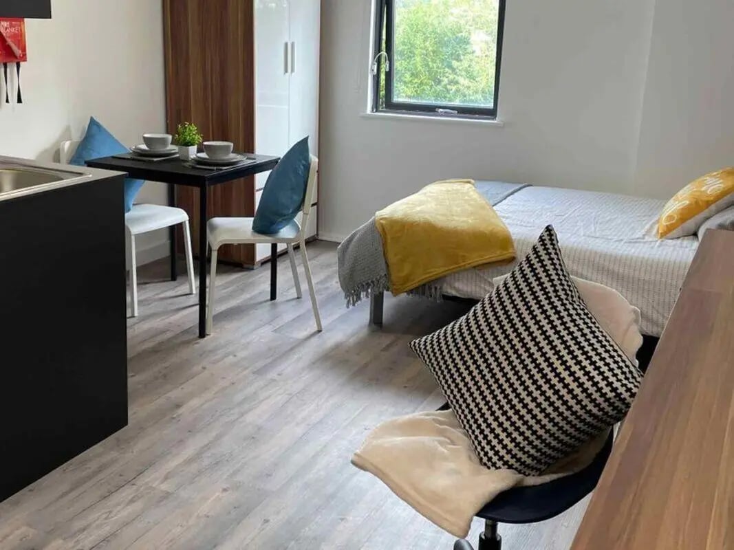 Table chairs bed pillows wardrobe window bedroom at Asquith House in Leeds Student Accommodation