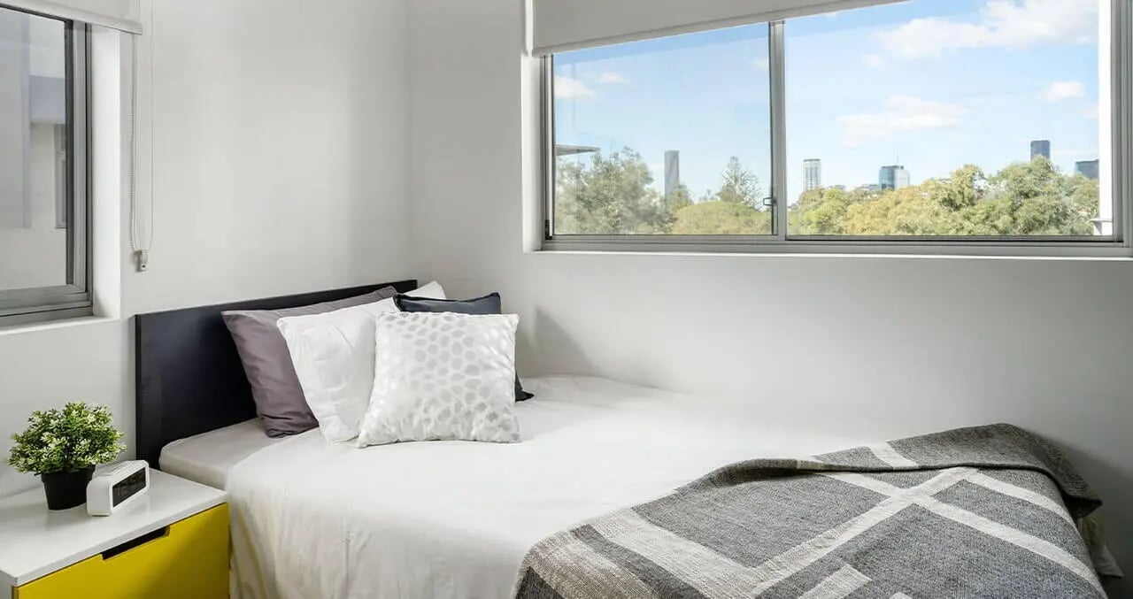 Bed with pillows plants clock and city view bedroom at Iglu Kelvin Grove in Brisbane Student Accommodation