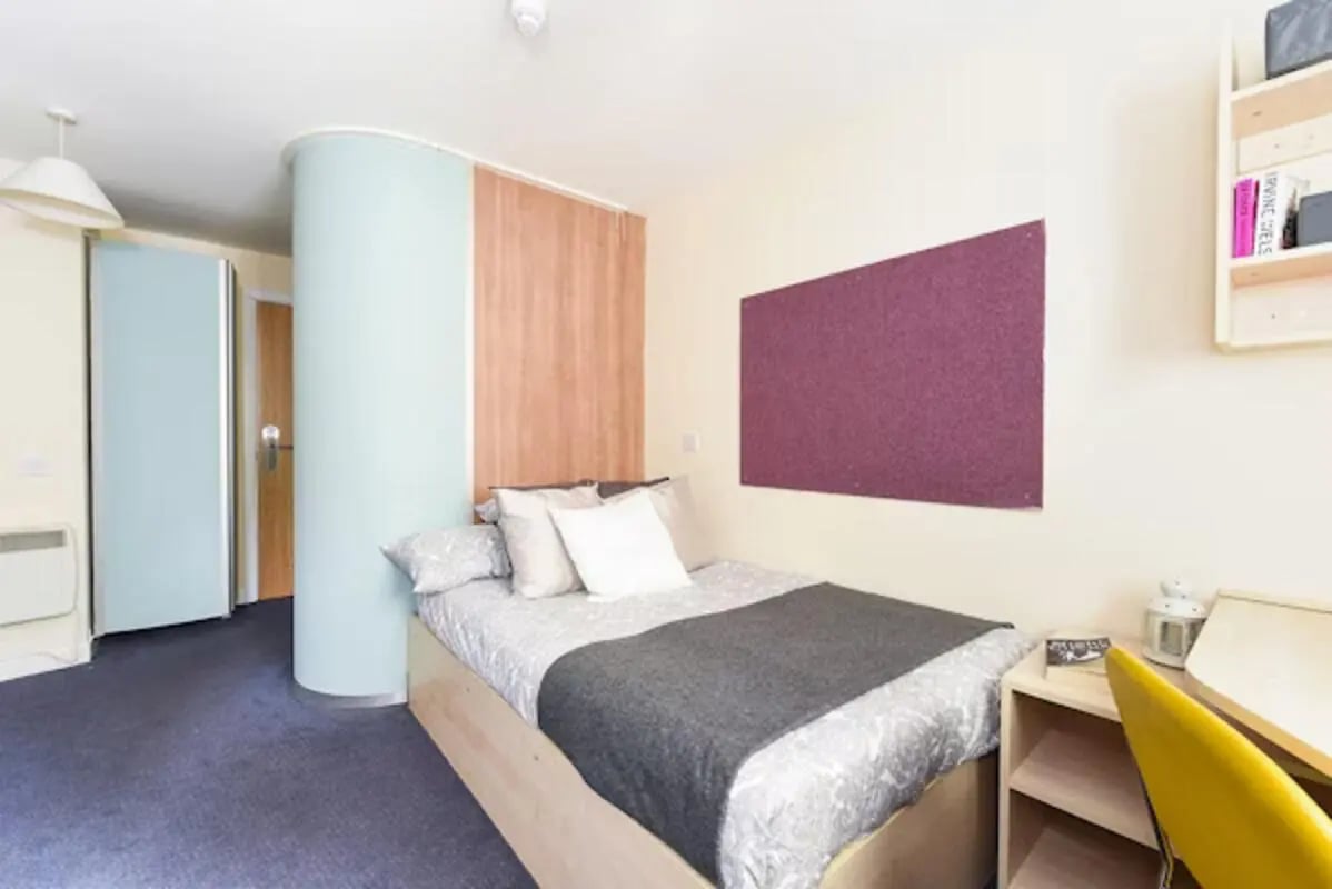 Bed with pillows desk with yellow chair and corkboard Bedroom at Gibson Street in Glasgow Student Accommodation