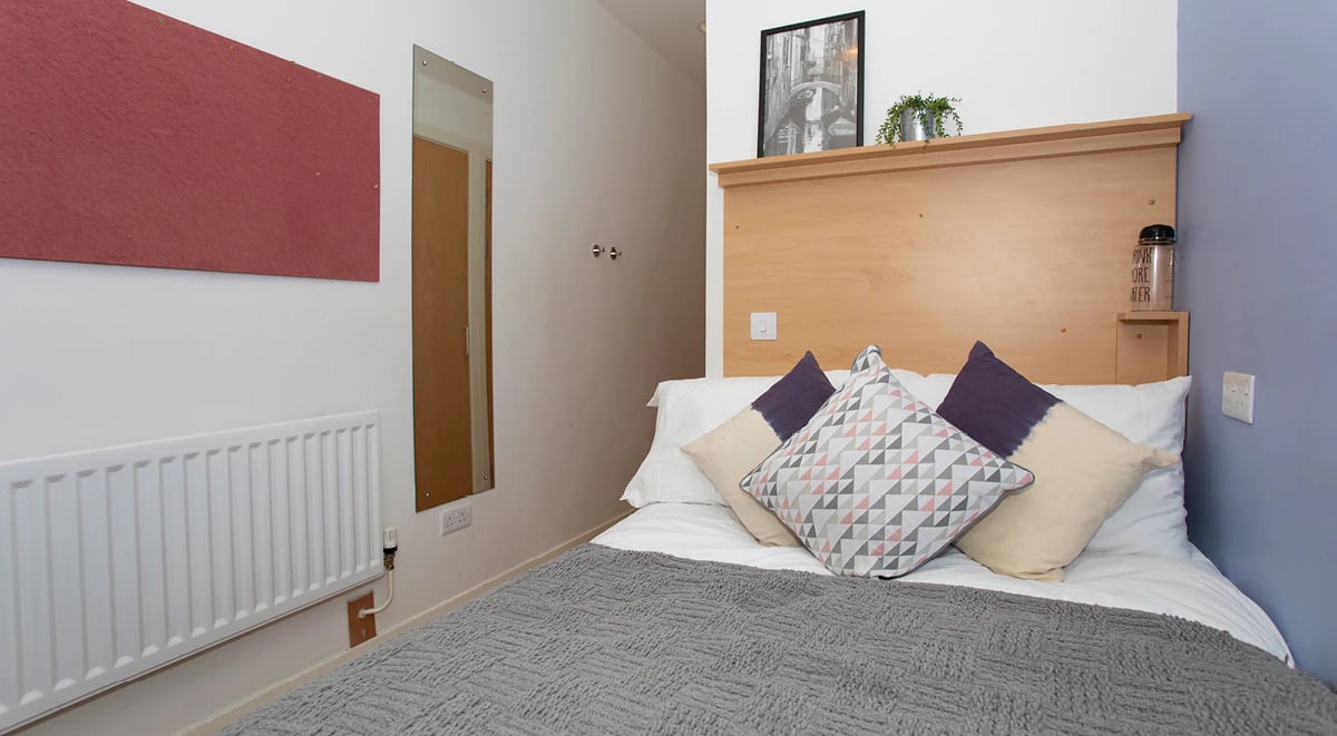 Bed with patterned pillows and grey throw Bedroom at 200 Cowgate in Edinburgh Student Accommodation