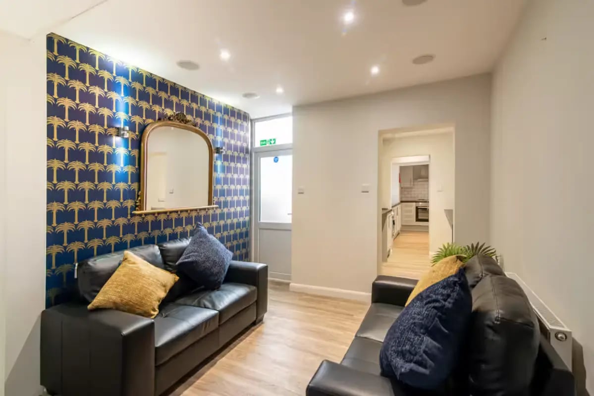 Black sofas with pillows, mirror, kitchen visible living room at 123 Leek Road in Stoke-On-Trent Student Accommodation