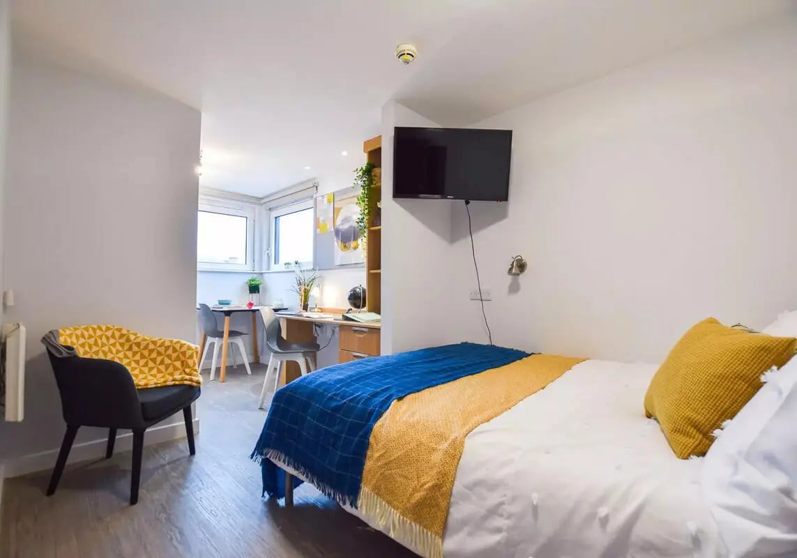 Bed with blue yellow throws desk chair television bedroom at iQ Steel in Sheffield Student Accommodation