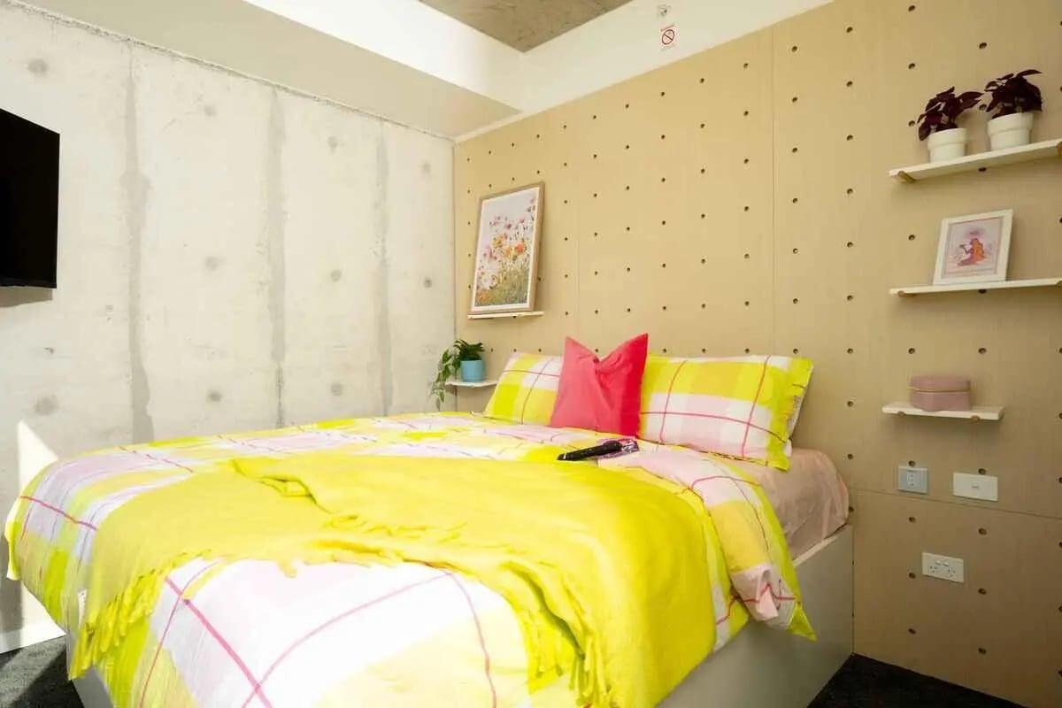 Bed with yellow throw pink pillows and framed art bedroom at Scape Kingsford in Sydney Student Accommodation