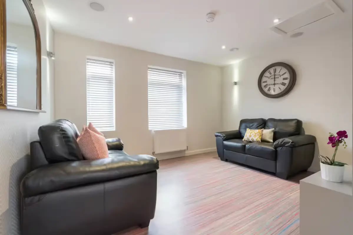 Two black sofas patterned pillows large clock living room at 16 Queen Anne Street in Stoke-On-Trent Student Accommodation
