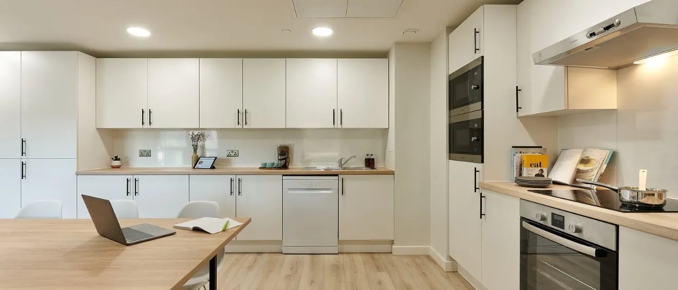 White cabinets appliances laptop and wooden table kitchen at Christchurch Road in Bournemouth Student Accommodation