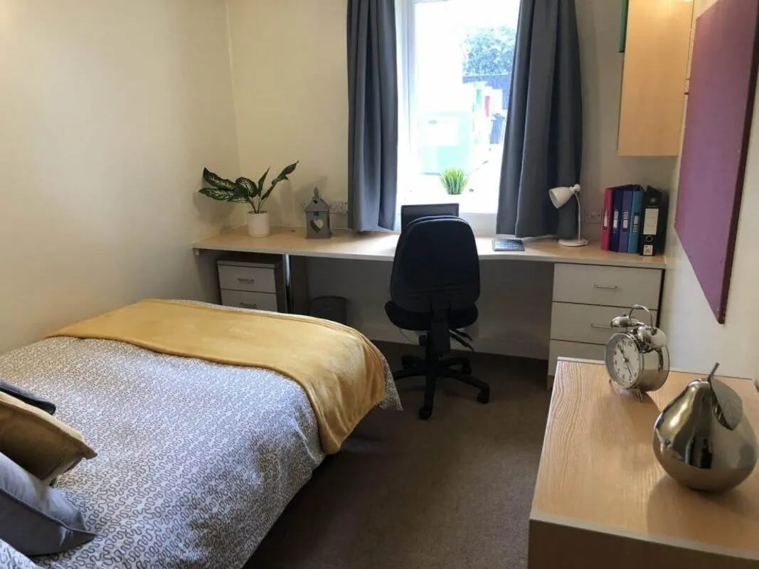 Bed desk chair plant folders alarm clock bedroom at Horton House Bradford in Bradford Student Accommodation