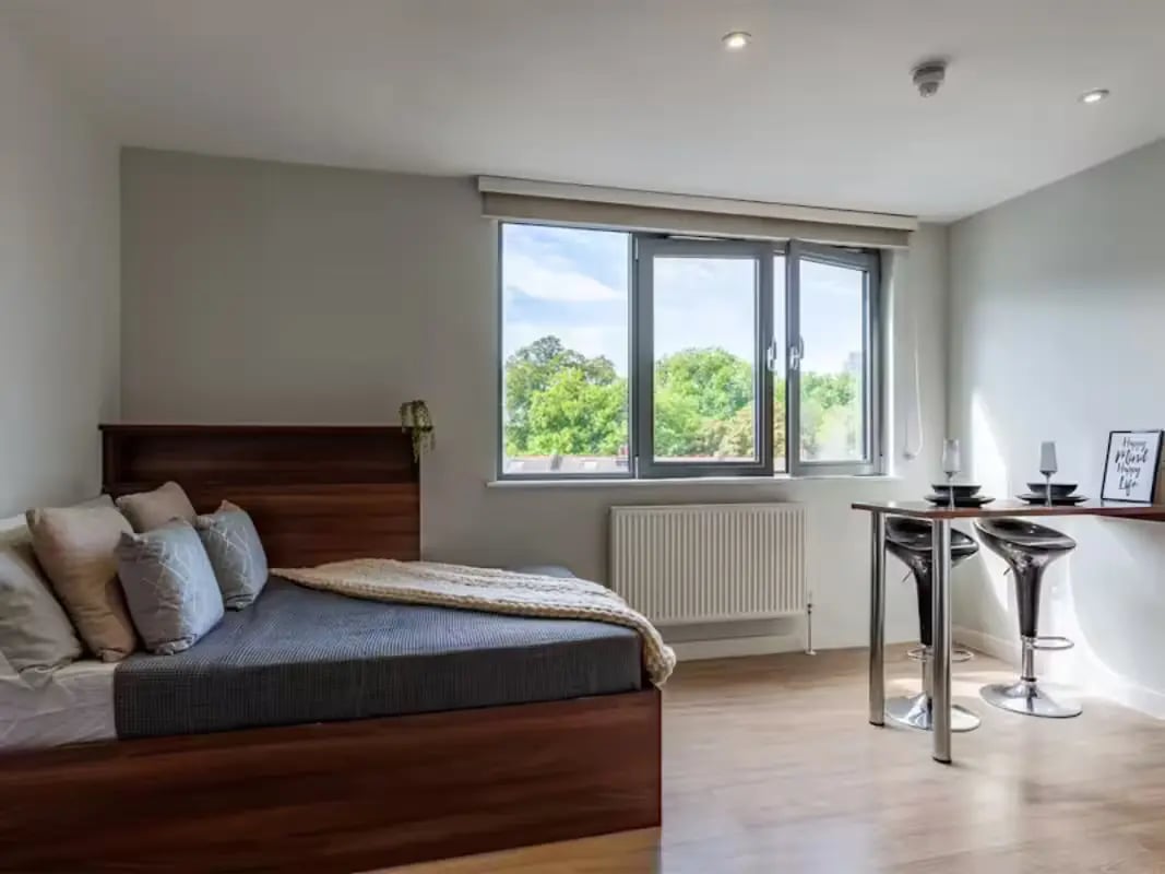 Bed with pillows and a throw next to a table. at Central Studios - London in London Student Accommodation