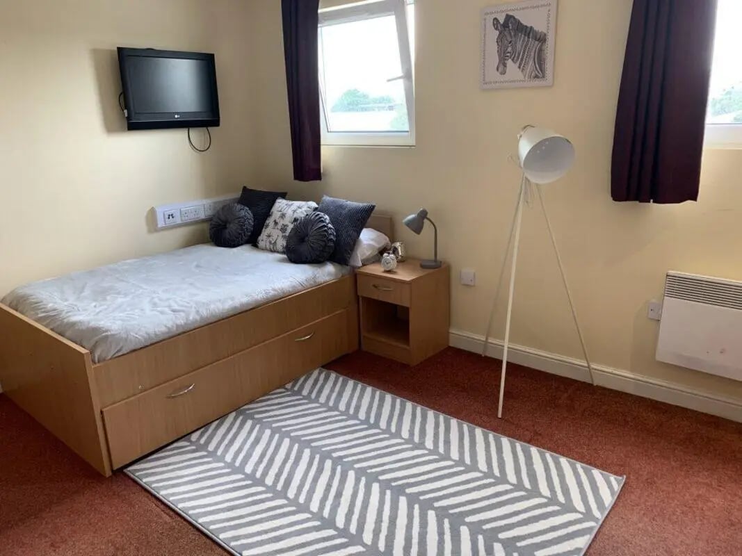 Bed with drawers bedside table lamp rug and TV bedroom at Longside House Bradford in Bradford Student Accommodation