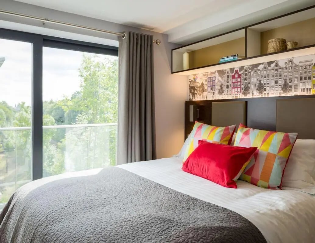 Bed with colorful pillows and large window bedroom at The Glassworks - Leeds in Leeds Student Accommodation