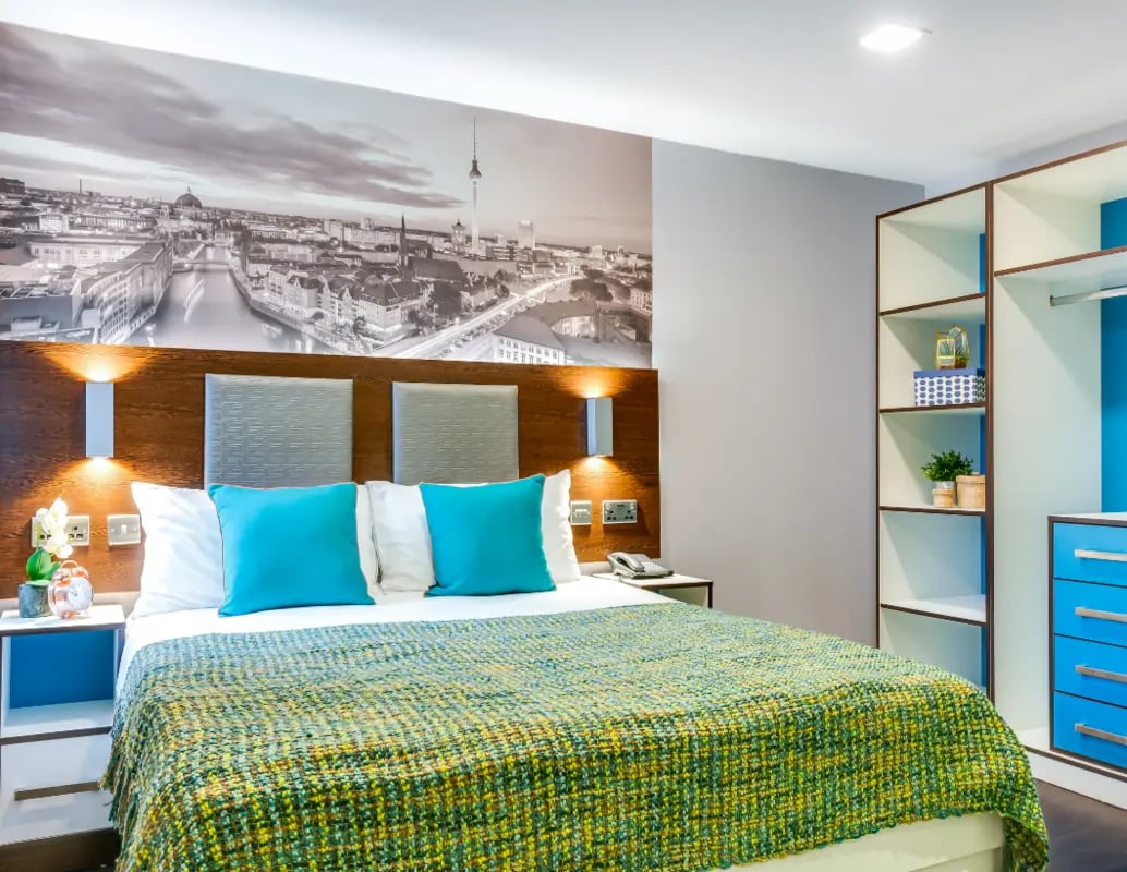 Bed with teal pillows green blanket cityscape mural bedroom at The Edge - Leeds in Leeds Student Accommodation
