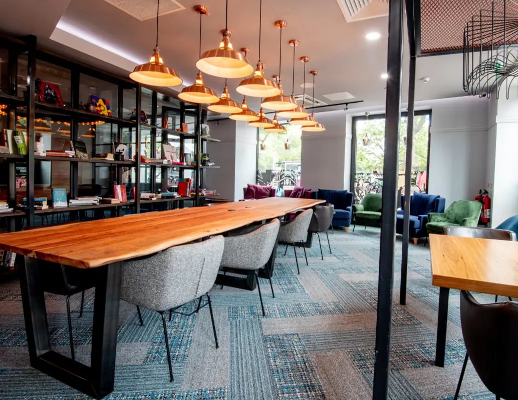 Long wooden table grey chairs bookshelves seating area lounge at IconInc London Stratford in London Student Accommodation