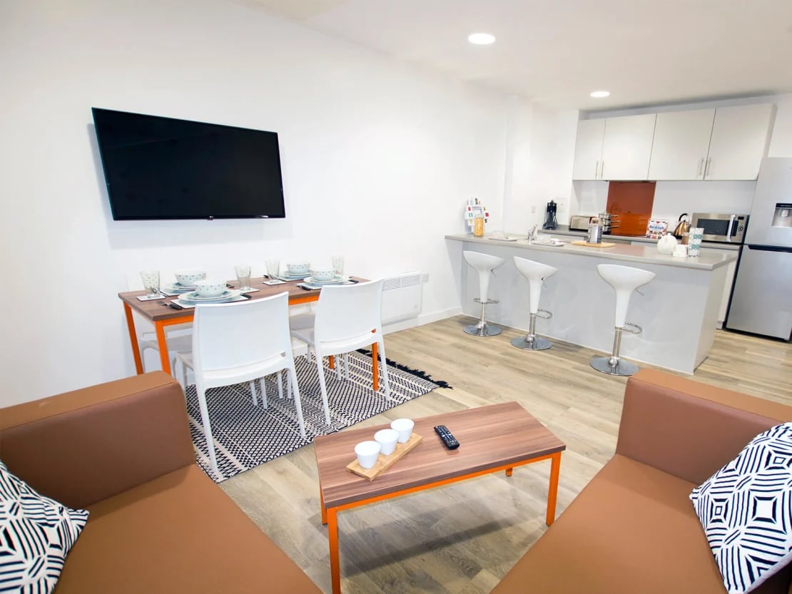 Dining table white chairs television kitchen living area living room at The Shield in Newcastle Upon Tyne Student Accommodation