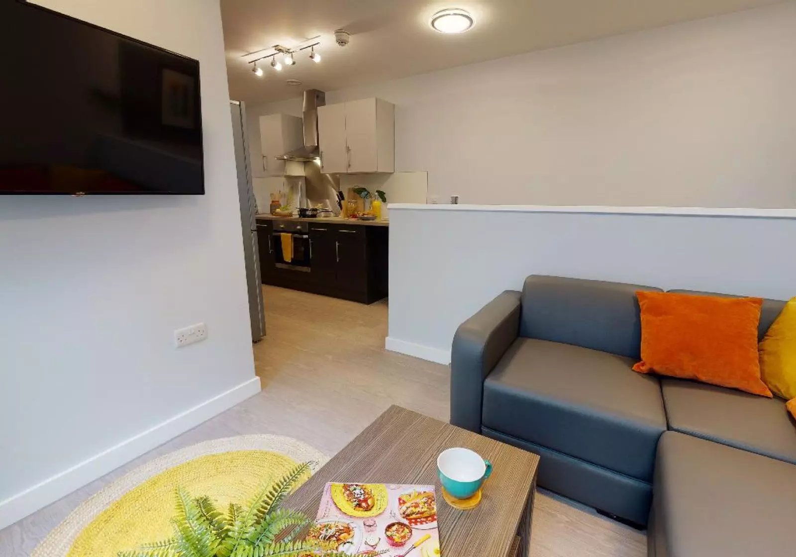 Grey sofa orange pillow coffee table kitchen living room at iQ Will Wyatt Court in London Student Accommodation