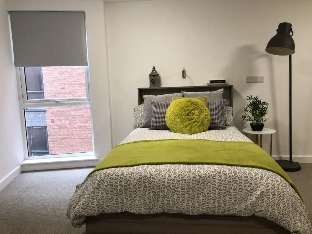 Bed with green throw and yellow pillow bedroom at Q Studios in Stoke-On-Trent Student Accommodation