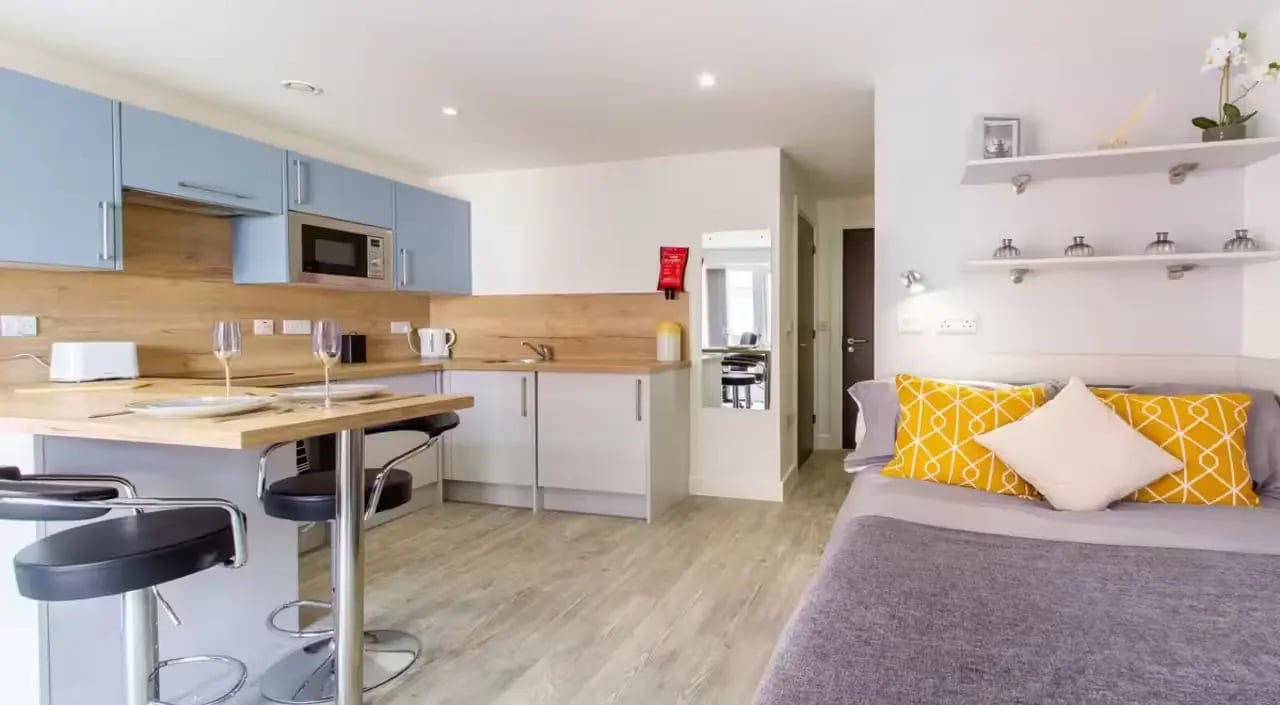 Kitchenette with bar stools bed and yellow pillows studio at Dover Street Apartments in Leicester Student Accommodation