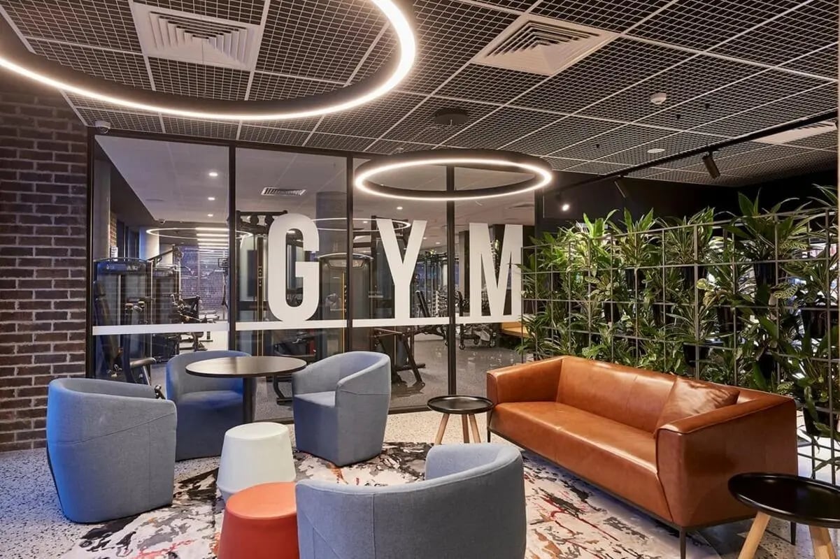 Lounge area with seating and gym visible beyond Living room at Scape Queensberry in Melbourne Student Accommodation