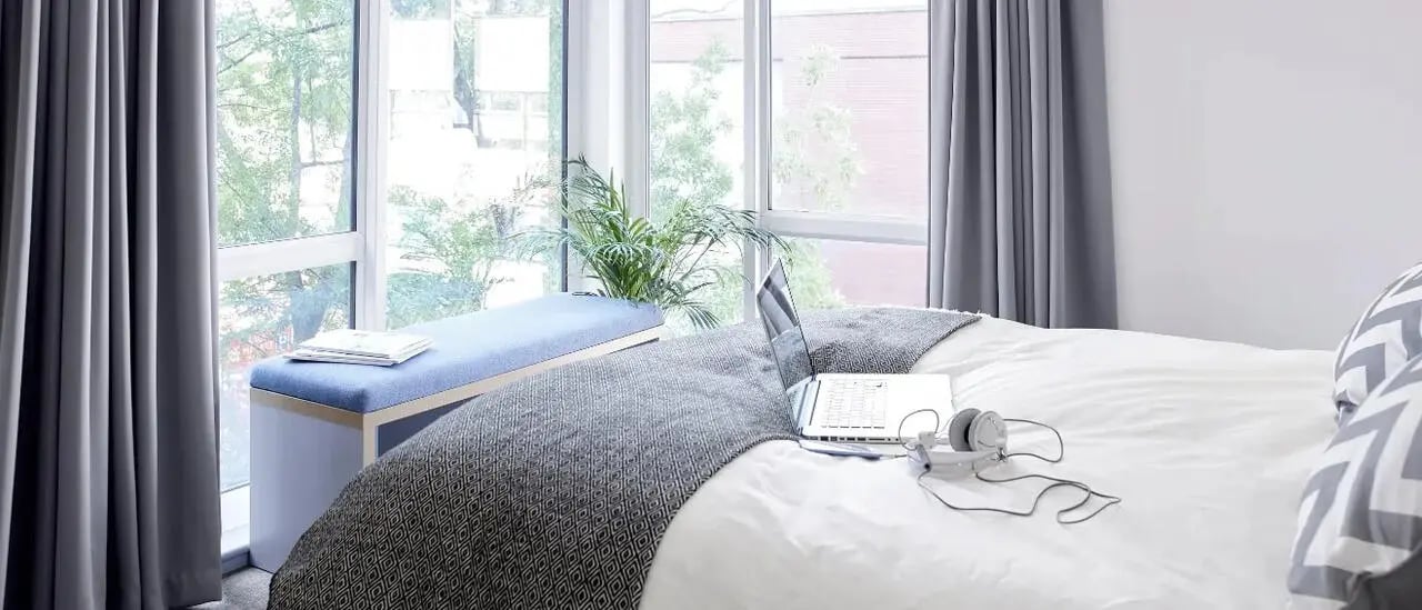 Bed with laptop headphones bench window Bedroom at Lace Market Studios in Nottingham Student Accommodation