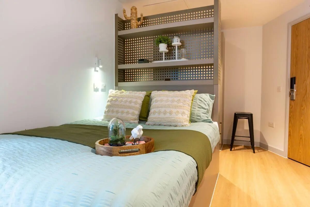 Bed with pillows shelves cactus stool Bedroom at Market Quarter Studios in Bristol Student Accommodation