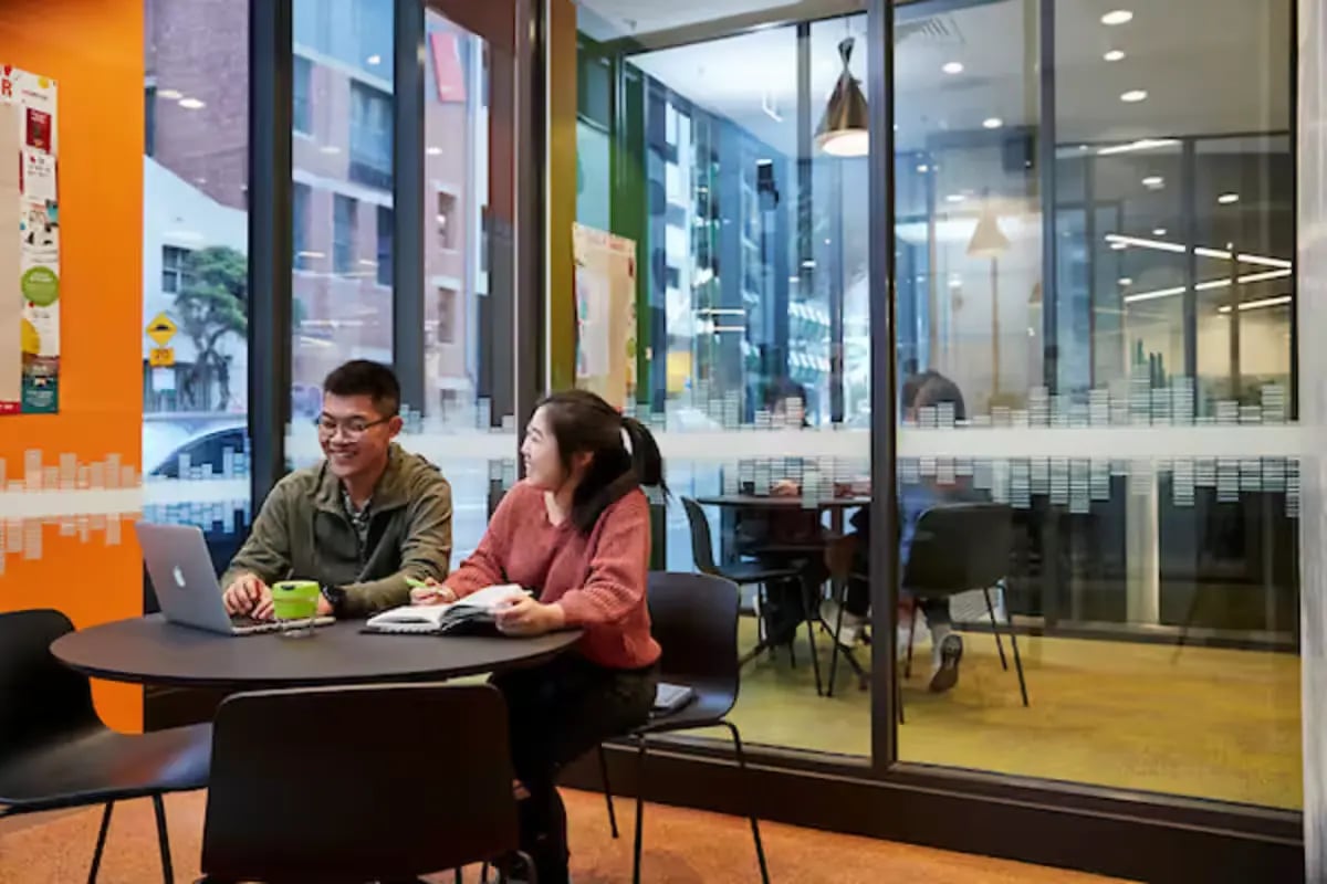 Students at table with laptop and book common area at Scape Berkeley 2 in Melbourne Student Accommodation
