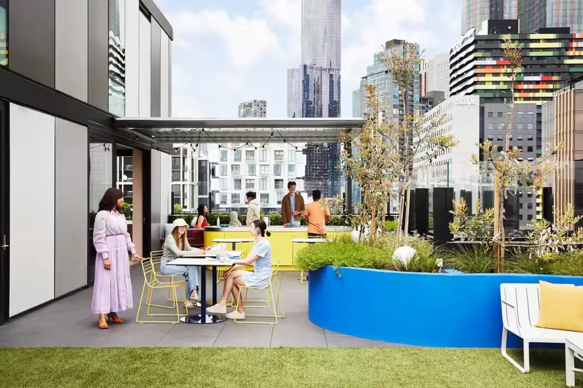 Students socializing at rooftop patio tables and kitchen area at Scape Lincoln College in Melbourne Student Accommodation
