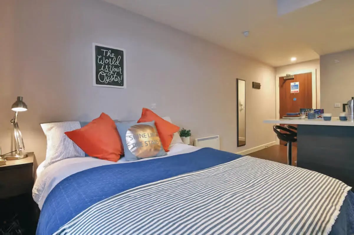 Bed with orange pillows desk lamp and bar counter bedroom at Talbot Studios in Nottingham Student Accommodation