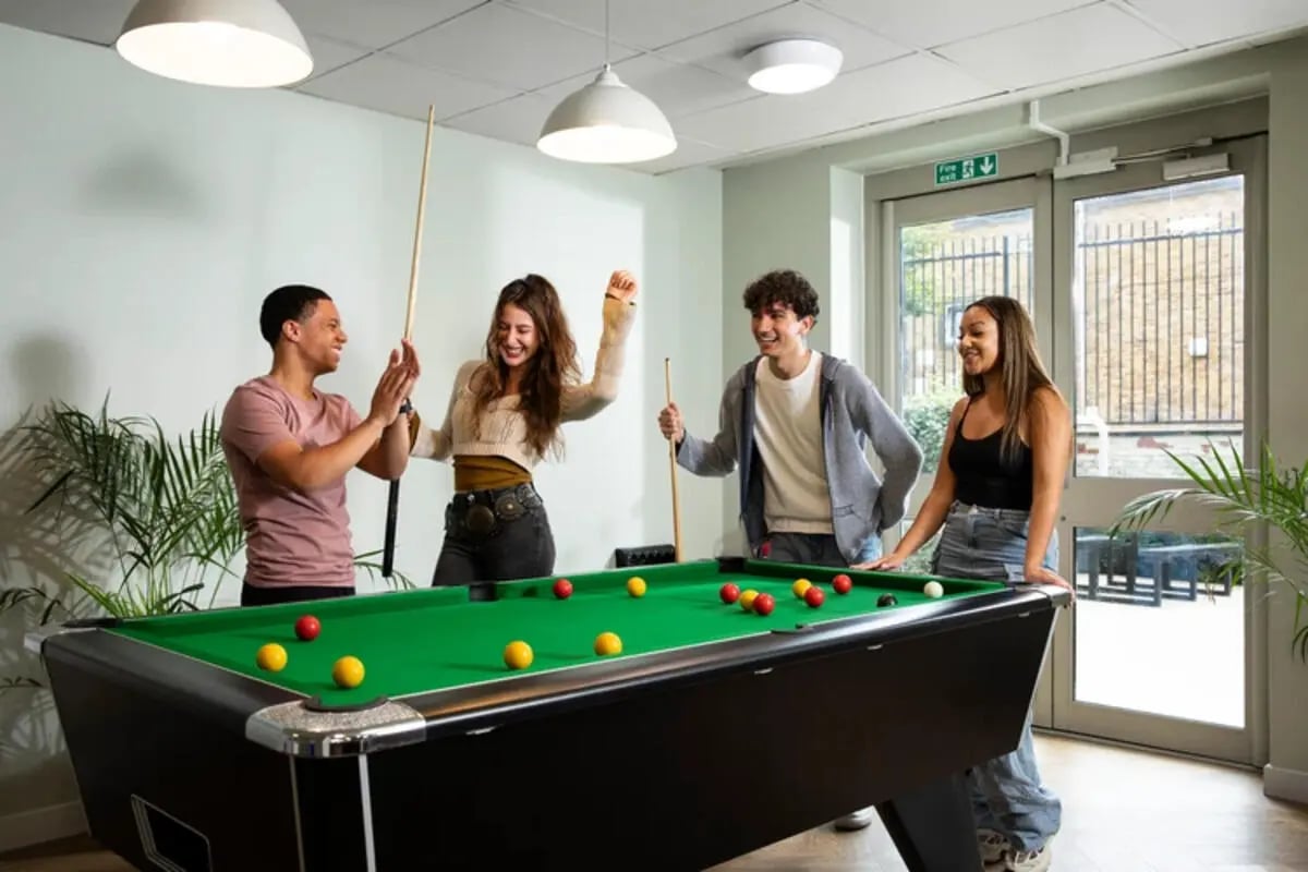 Four students playing pool by large doors common room at Quantum Court in London Student Accommodation