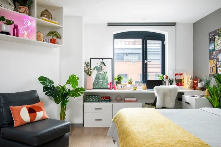 Bed with yellow blanket armchair desk and plants Bedroom at Brunel House in Bristol Student Accommodation