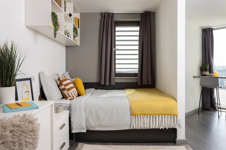 Bed with pillows and yellow blanket beside desk bedroom at Newgate Court in Newcastle Upon Tyne Student Accommodation