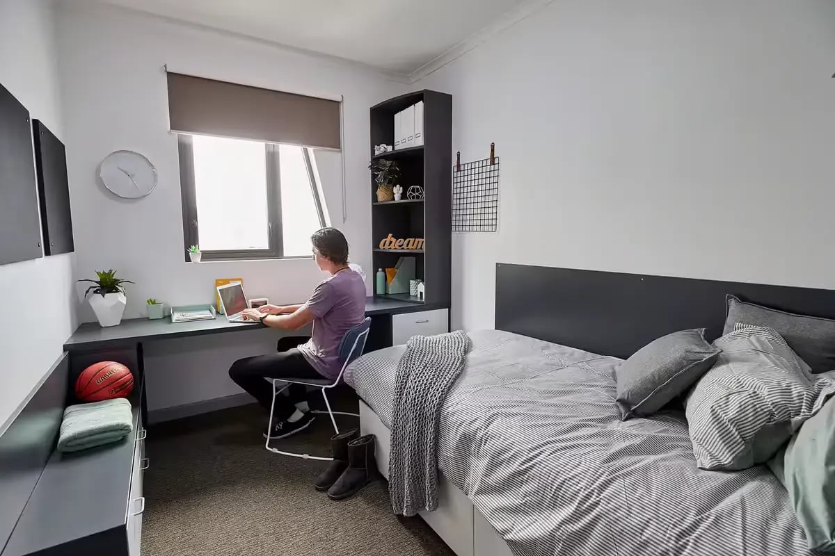 Student working at desk near bed bedroom at Scape Tribune in Brisbane Student Accommodation