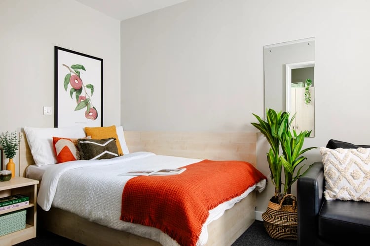 Bed with orange blanket and plants bedroom at Raglan House in Coventry Student Accommodation