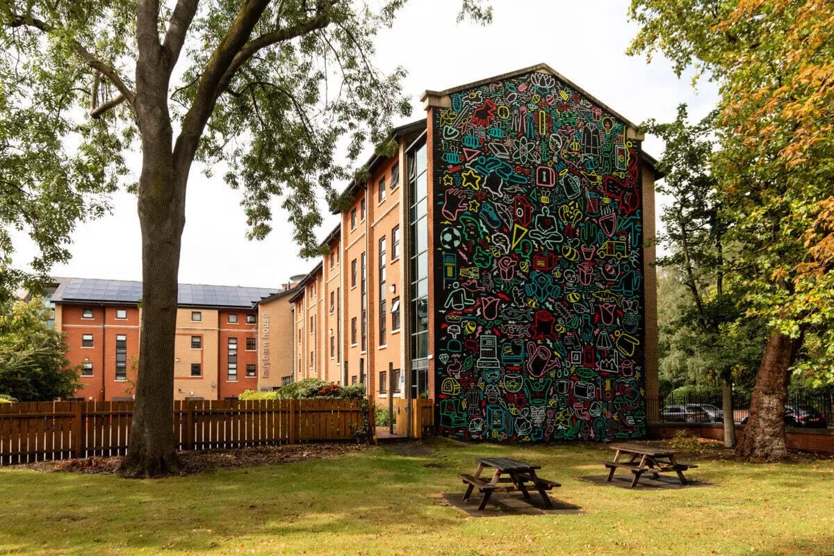 Student accommodation with mural and picnic tables exterior at Ladybarn House in Manchester Student Accommodation