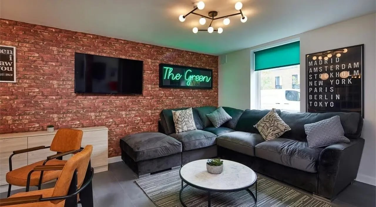 Dark sectional couch coffee table neon sign living room at The Green in Bradford Student Accommodation