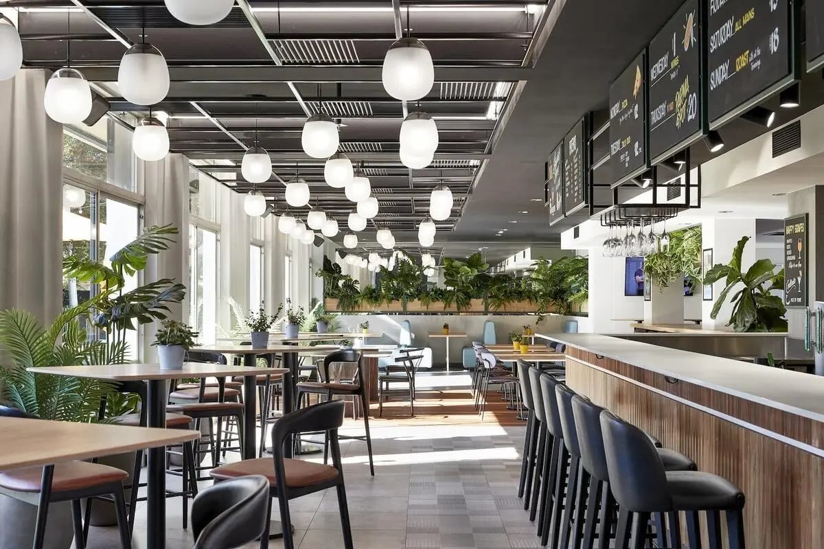 Tables chairs plants and bar area communal space at Campus Melbourne in Melbourne Student Accommodation