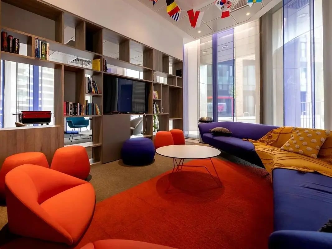 Modern lounge area with blue couch and orange chairs. at Felda House in Wembley Student Accommodation