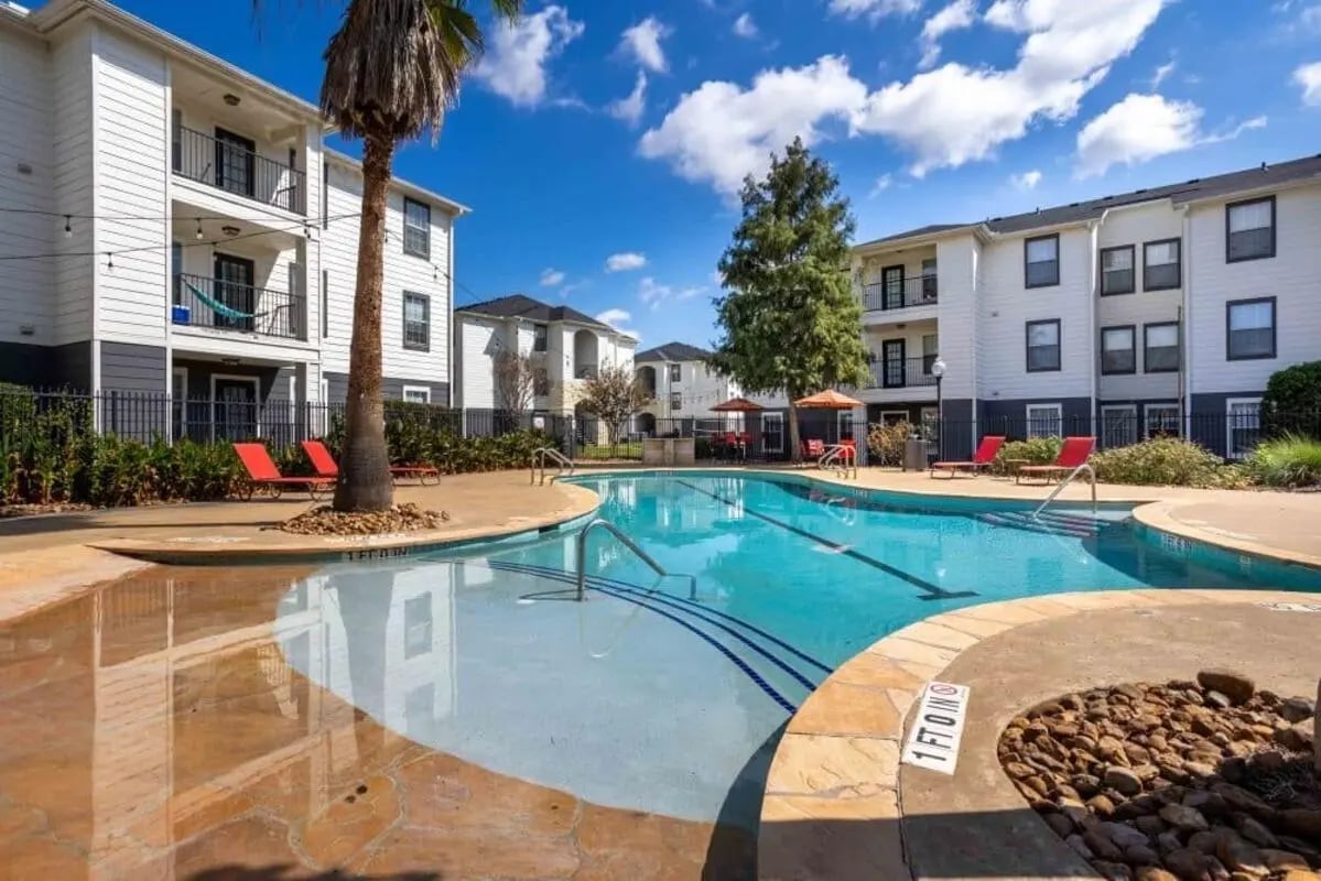 Swimming pool with lounge chairs and apartment buildings exterior at Crossing Place in College Station Student Accommodation