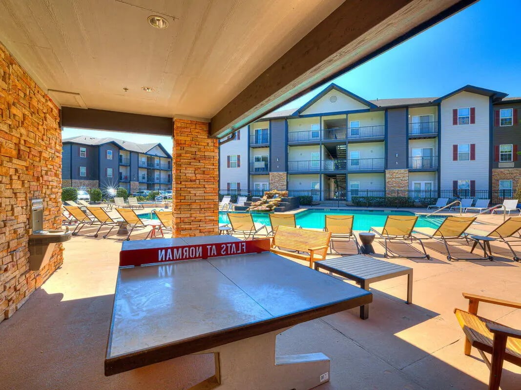 Ping pong table poolside with lounge chairs exterior at The Flats at Norman in Norman Student Accommodation