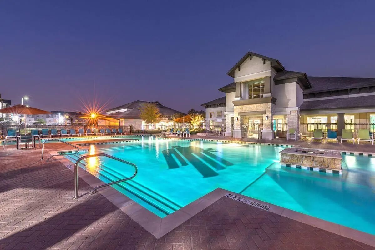 Illuminated swimming pool with lounge chairs and building exterior. at Forum at Denton Station in Denton Student Accommodation