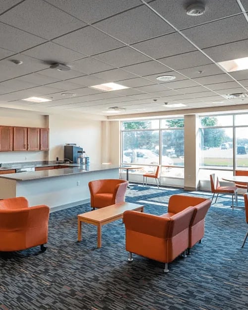 Orange chairs coffee table kitchen counter lounge area at Campus Walk Apartments in Buffalo Student Accommodation