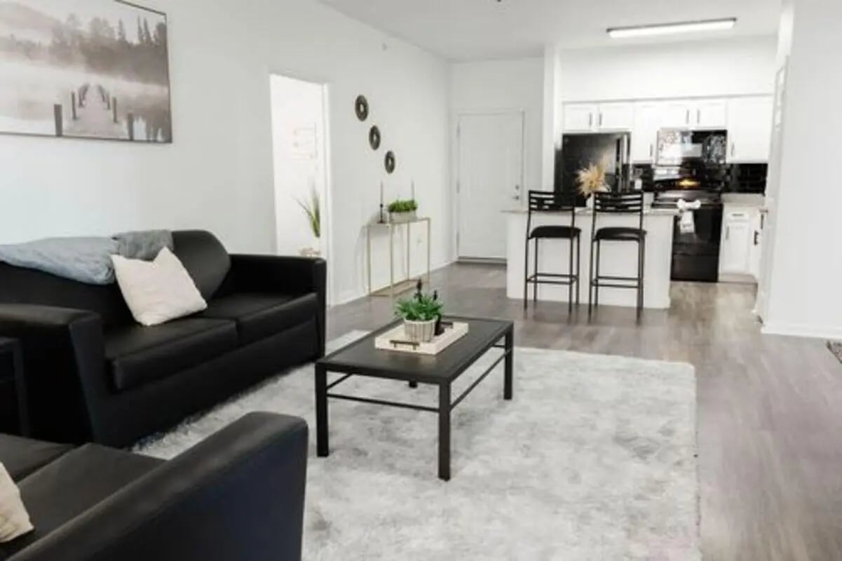 Black couches coffee table rug kitchen living room at Villagio Apartments in San Marcos Student Accommodation