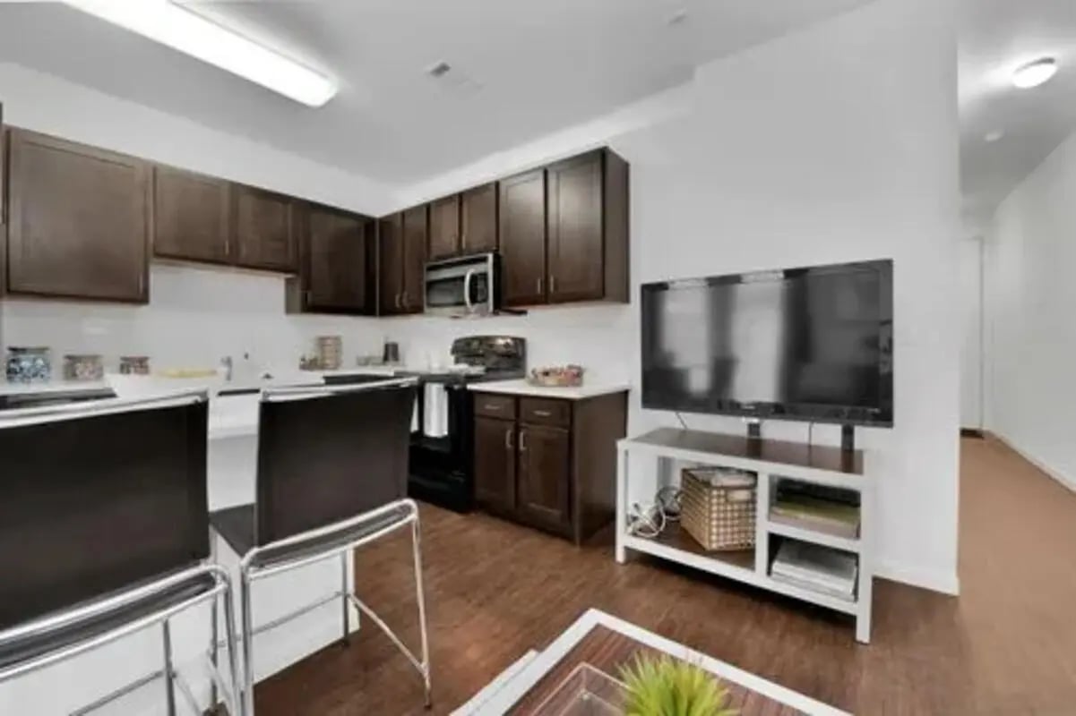 Dark cabinets kitchen island two bar stools TV living room at GrandMarc Austin in Austin Student Accommodation