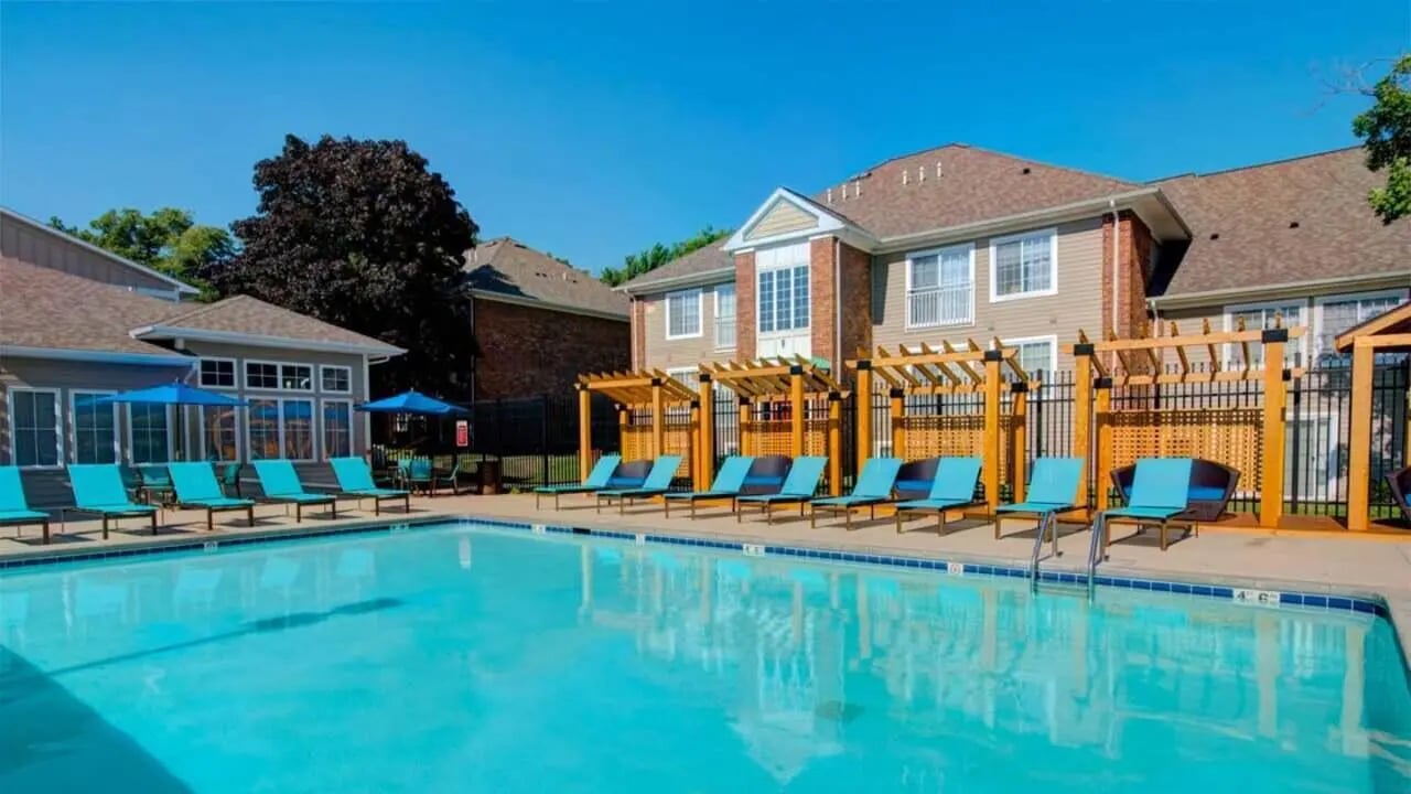 Poolside loungers and umbrellas with apartment buildings exterior at Knollwood Apartments in Kalamazoo Student Accommodation