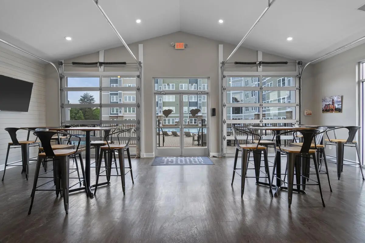 Tables and chairs with garage doors opening to pool area at The Ridge Clemson in Central Student Accommodation