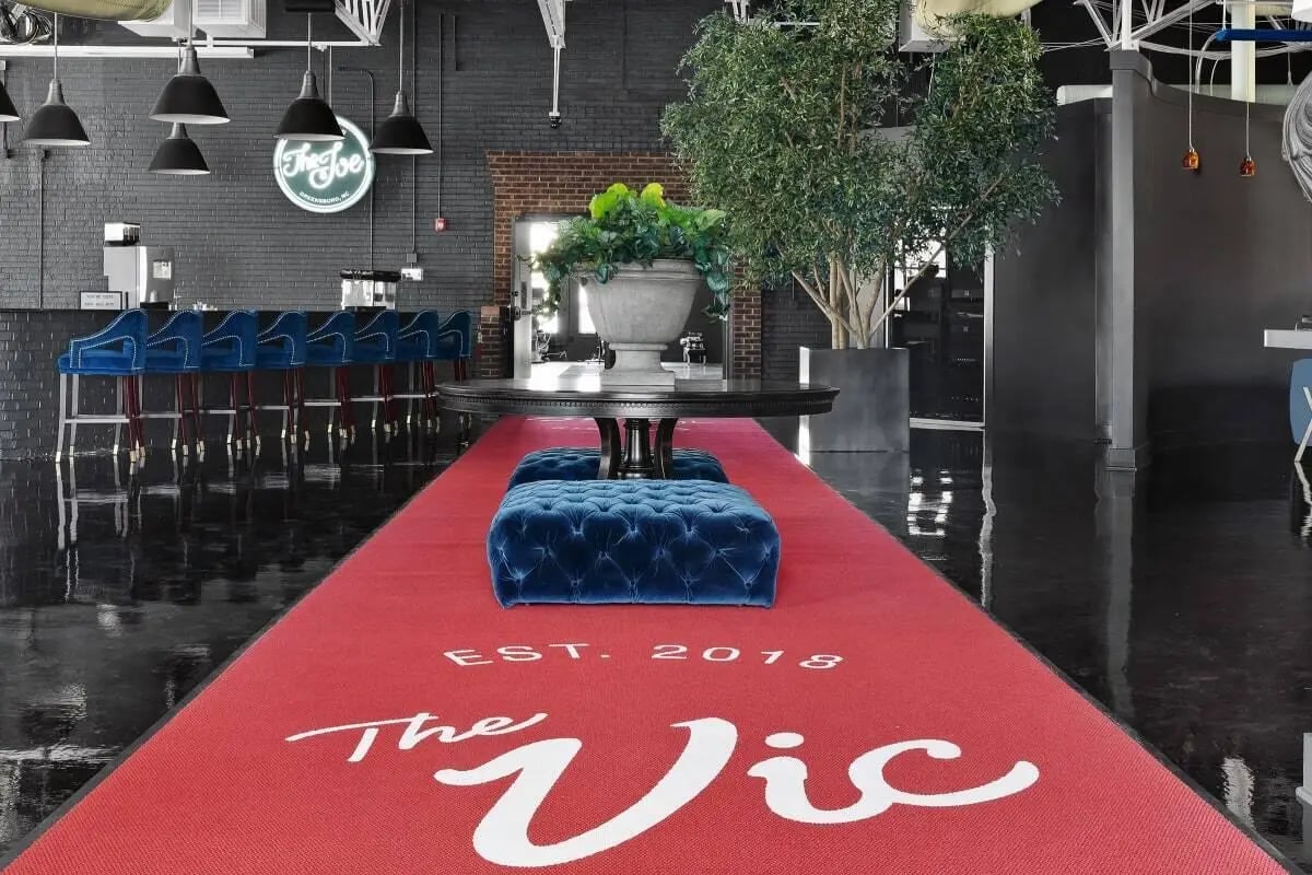 Red carpet with blue tufted ottomans and bar stools common area at The Vic in Greensboro Student Accommodation
