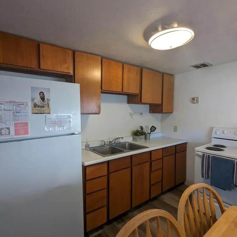 Refrigerator sink cabinets stove wooden chairs kitchen at Crestwood Rexburg Apartments in Rexburg Student Accommodation